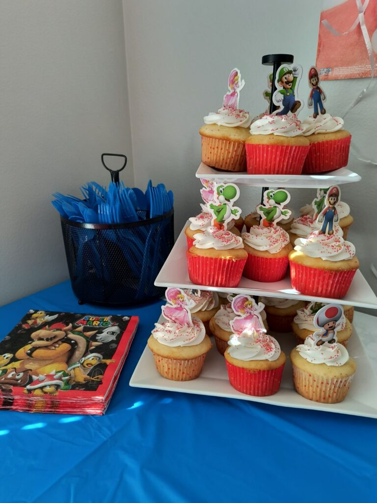 Mario bros party cupcakes with character cutout toppers on tiered platter with Bowser napkins next to it
