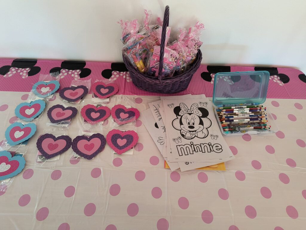 Minnie Mouse birthday craft table with foam hearts, Minnie coloring pages, and a purple basket with party favors