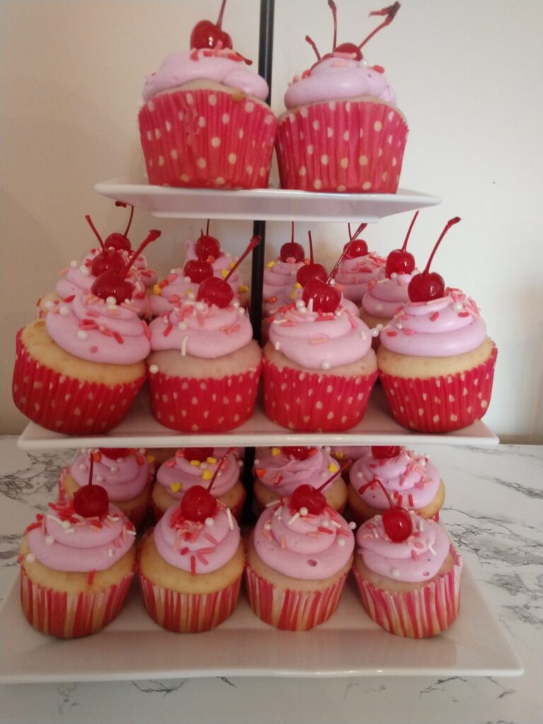 Pinkalicious birthday cupcakes in printed wrappers with cherries on top displayed on white serving stand